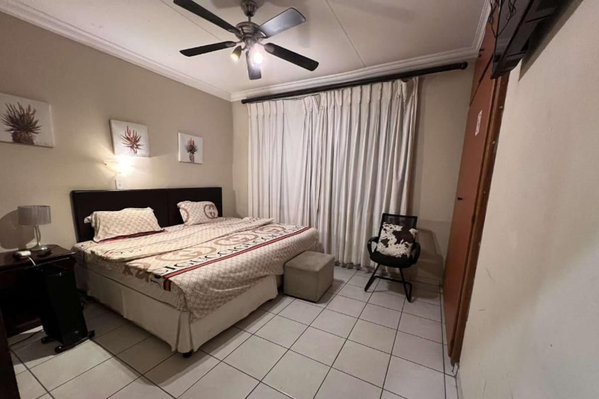 A bedroom with a bed, a chair, a ceiling fan, and curtains.