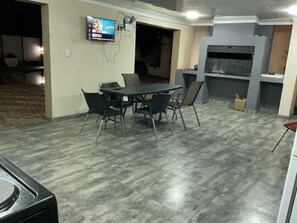 A dining area with a table and chairs, a flat-screen TV mounted on the wall, and a built-in oven. - Los Angeles Gueshouse (Benoni)