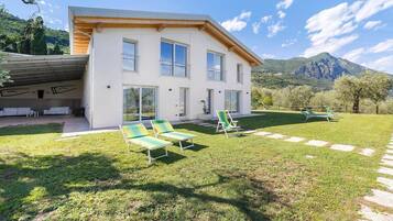 A modern two-story house with a covered garage, a grassy lawn, and a mountain backdrop.