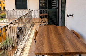 Une table en bois, entourée de chaises, sur un balcon doté d’une rambarde en métal.
