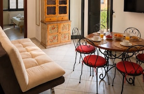 Un coin repas avec une table ronde, des chaises rembourrées de couleur rouge et une table préparée pour le petit-déjeuner, avec du jus d’orange et des viennoiseries.