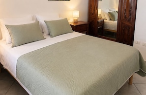 Un lit bien fait, avec une couverture verte et des oreillers, une table de chevet avec une lampe et une armoire en bois.