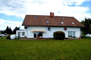 Einbungalow mit einem Ziegeldach, einer kleinen Veranda mit zwei Stühlen und einer Satellitenschüssel.