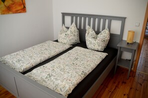 Ein Doppelbett mit grauer Kopfteil und blumigem Bettzeug, ein Nachttisch mit Lampe und Holzboden.