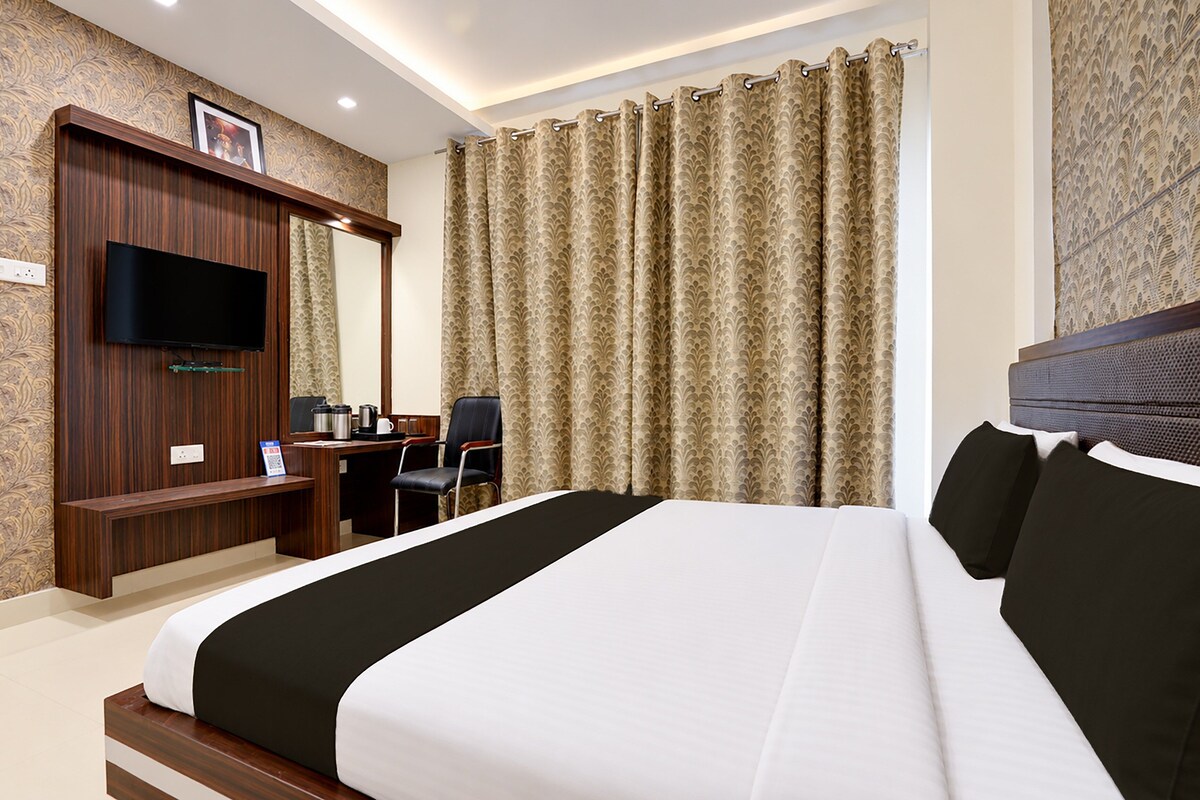 A hotel room with a large bed, a desk with a chair, a television, and curtains.
