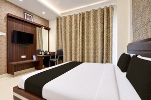 A hotel room with a large bed, a desk with a chair, a television, and curtains. - Townhouse Sankat Mochan Hanuman Temple (Varanasi)