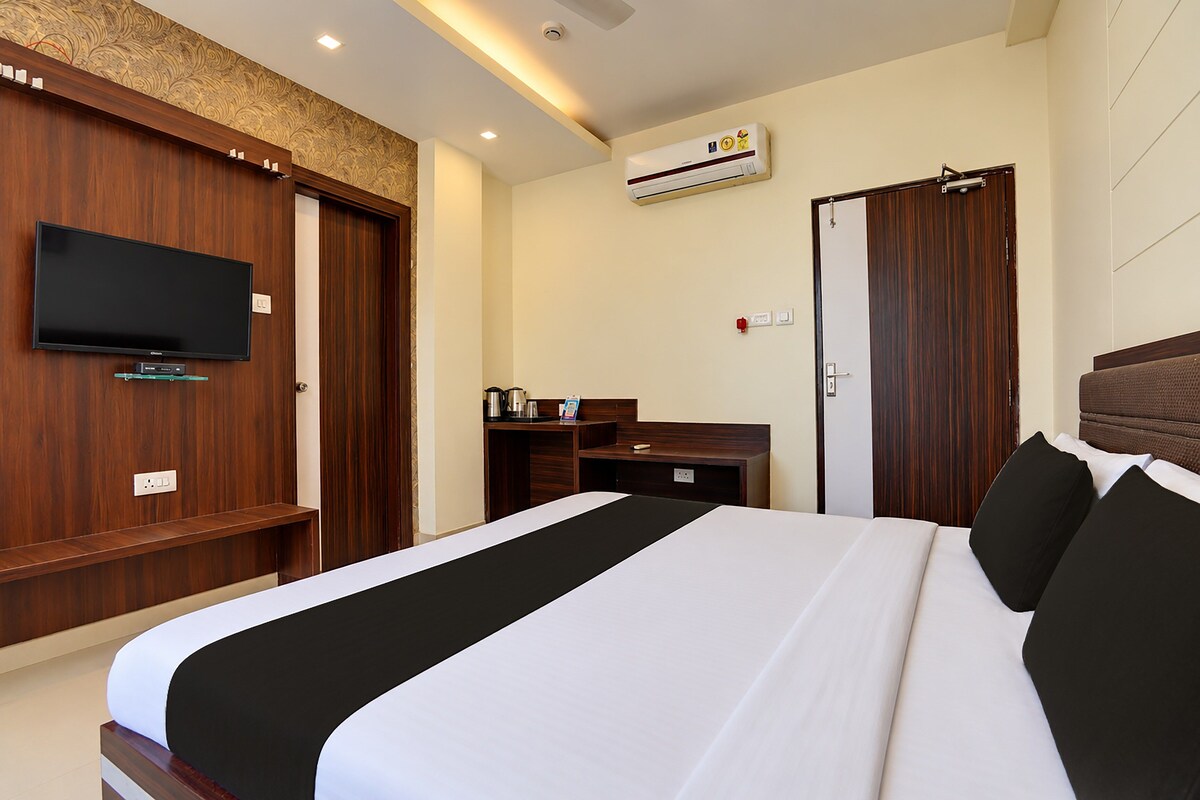 A hotel room with a bed, a television, a desk, a wardrobe, and an air conditioning unit.