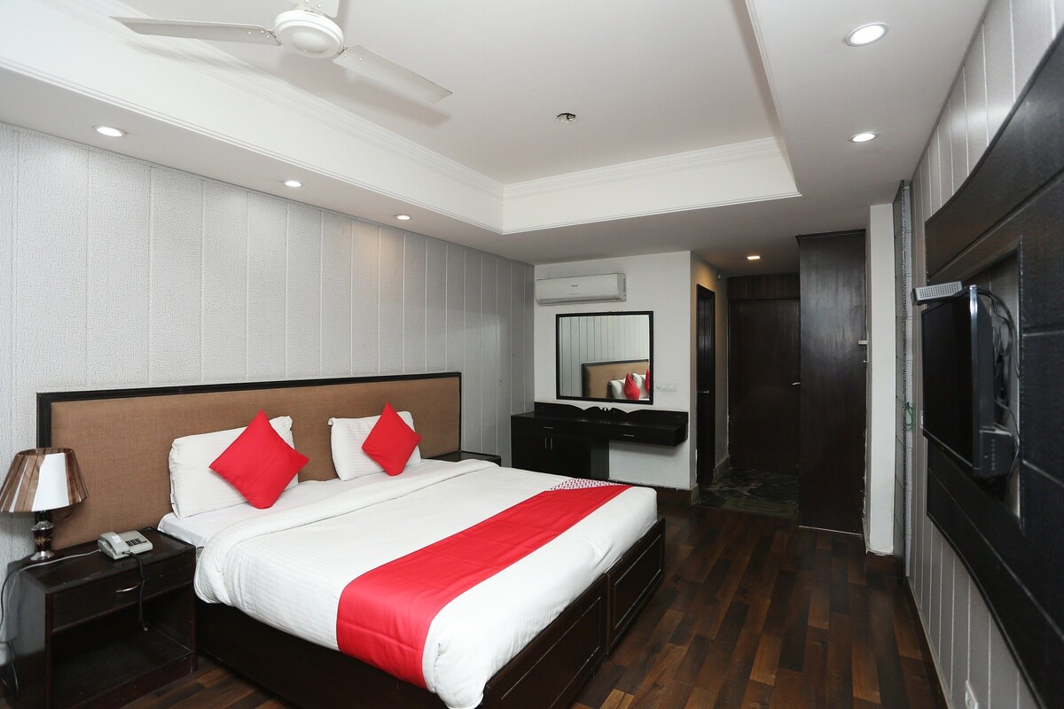 Habitación de hotel con cama, mesita de noche, lámpara y ventilador de techo.