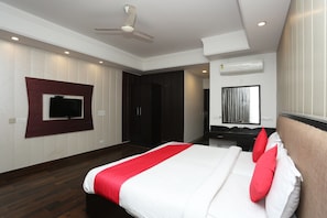 Habitación de hotel con cama, televisor montado en la pared, ventilador de techo, equipo de aire acondicionado y espejo con cortinas.