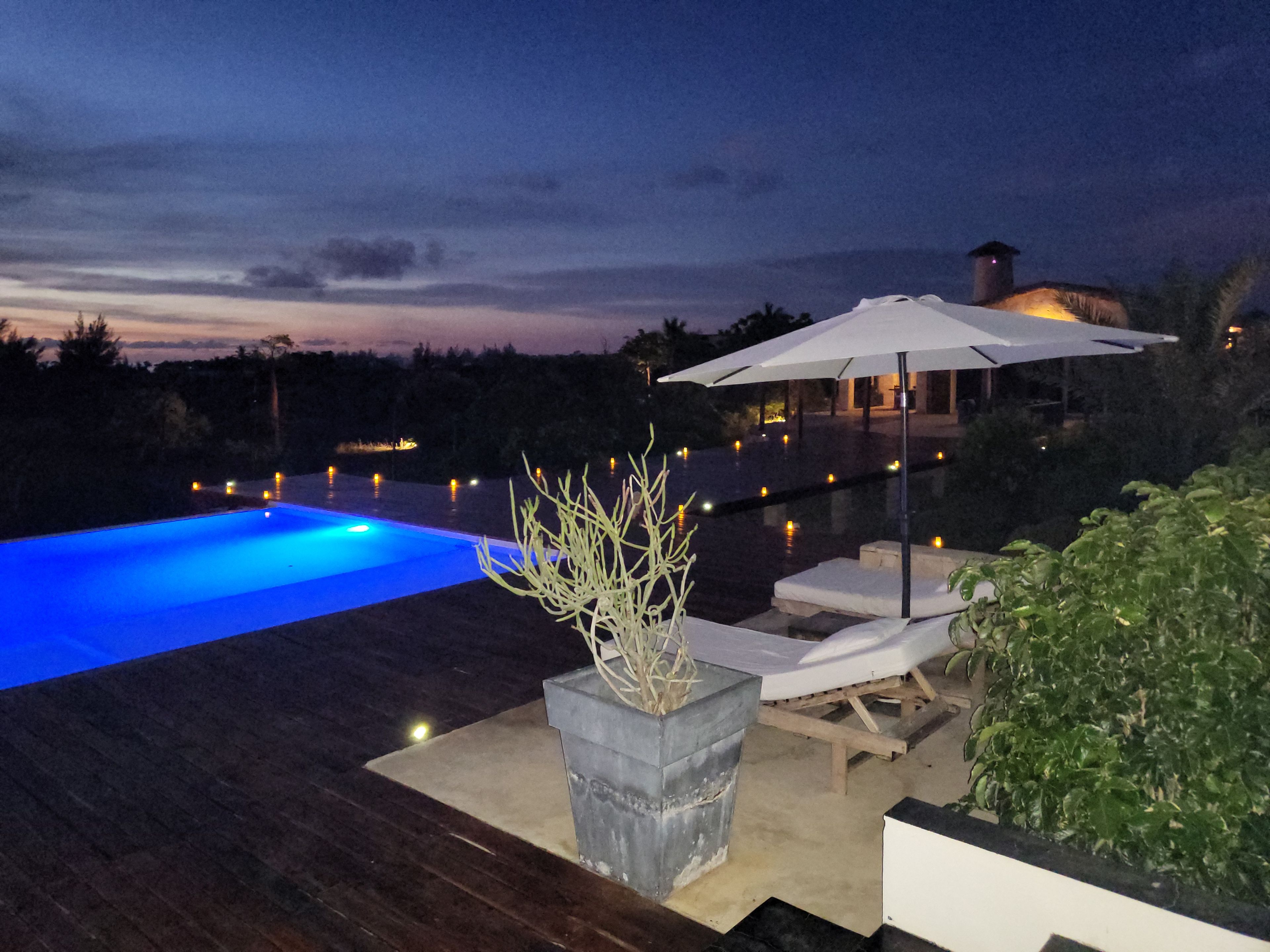 A swimming pool with a wooden deck, lounge chairs, and an umbrella.