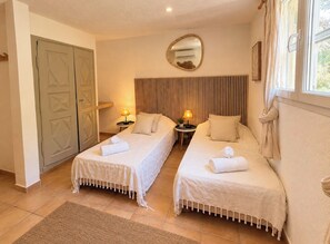 Een hotelkamer met twee eenpersoonsbedden, een grote spiegel, een raam met gordijnen en een deur met een geometrisch patroon.