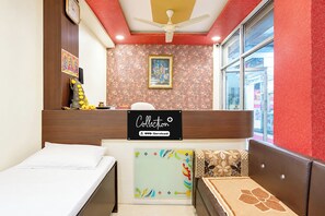 Habitació d'hotel amb un llit, una taula petita, un sofà, un ventilador de sostre, una finestra i una paret amb un quadre.