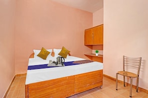A single bed with a wooden frame, a small bedside table, a chair, and a cabinet in a room with peach-colored walls. - Hotel O Prem Nagar Dehradun (Dehradun)