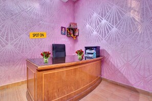 A reception desk with a pink patterned wall, a black chair, and two vases with red flowers. - Hotel O Prem Nagar Dehradun (Dehradun)