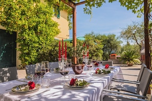 An outdoor dining area with tables set for a meal, surrounded by greenery and a building. - Tenuta Bellosguardo (Toscana)