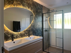 Une salle de bain moderne avec un grand miroir ovale, deux vasques, une douche en verre et un meuble-lavabo en bois.