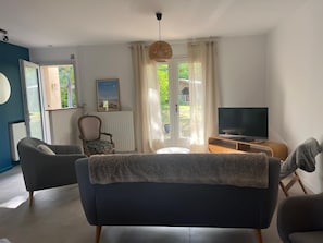 Un salon avec un canapé, un fauteuil, une télévision et une fenêtre avec des rideaux.
