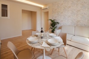 Un coin repas avec une table ronde dressée pour quatre personnes, un canapé et une plante en pot.
