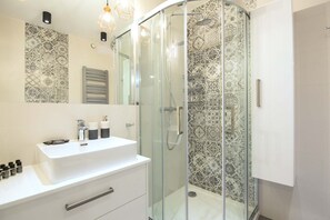 Ein modernes Badezimmer mit einer gläsernen Duschkabine, einem weißen Waschbecken mit Spiegel darüber und Wandfliesen mit Muster.