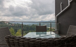 Ein Balkon mit Korbstühlen und einem Glastisch, mit Blick auf eine gebirgige Landschaft.
