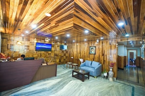 Een receptiezone met een houten plafond, een receptiebalie, een bank en een aan de muur bevestigde televisie.