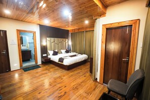 Een hotelkamer met een houten vloer, een bed met hoofdeinde, een nachtkastje, een stoel, een deur en uitzicht op de badkamer.