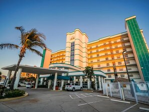 Een hotel met meerdere verdiepingen, een gebogen gevel, een centraal torentje en een parkeerplaats met overdekte ingang.