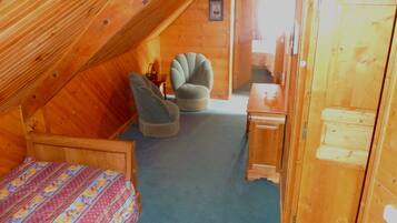 Ein gemütliches Schlafzimmer im Dachgeschoss mit einem Bett, zwei Stühlen, einem kleinen Tisch und einer Holztür.