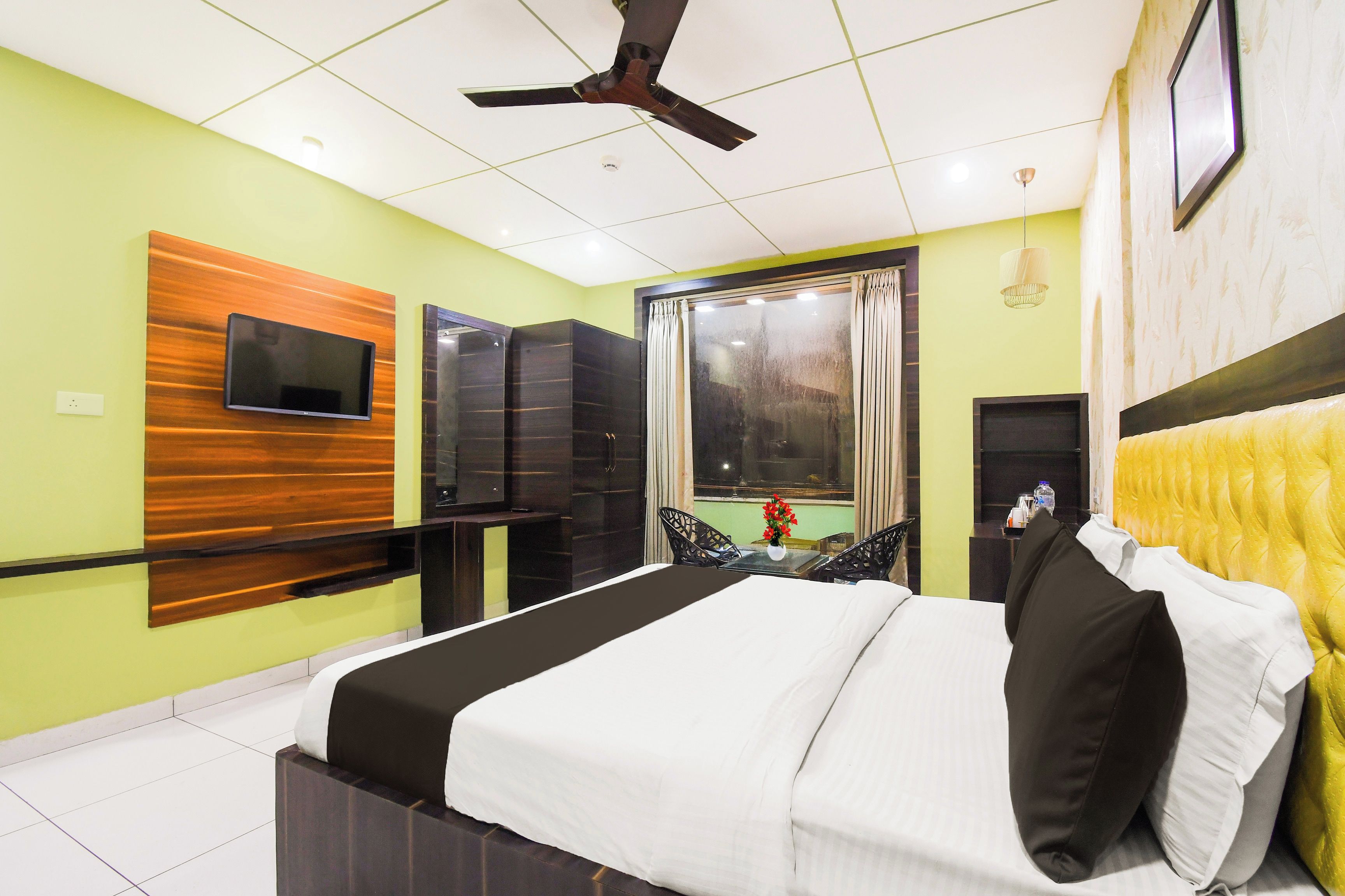 Une chambre d’hôtel équipée d’un lit, d’une télévision, d’un ventilateur de plafond et d’une fenêtre avec des rideaux.
