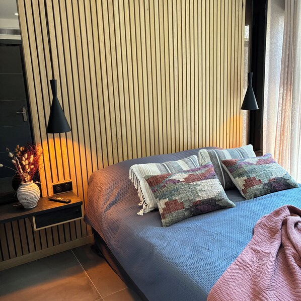 Une chambre moderne avec un mur en lambris de bois, une couvre-lit bleue et deux lampes suspendues noires.