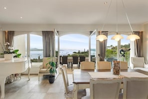 Ein Essbereich mit Meerblick, ein Balkon mit Tisch und Stühlen sowie ein weißer Konsolentisch mit Pflanze.
