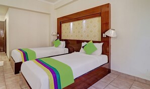 Une chambre d’hôtel avec deux lits, chacun agrémenté d’une couvre-lit colorée et de coussins, d’une tête de lit en bois, d’une lampe fixée au mur et d’un papier peint à motifs.