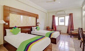 Une chambre d’hôtel avec deux lits, un bureau, une chaise, un appareil de climatisation et une fenêtre avec des rideaux.