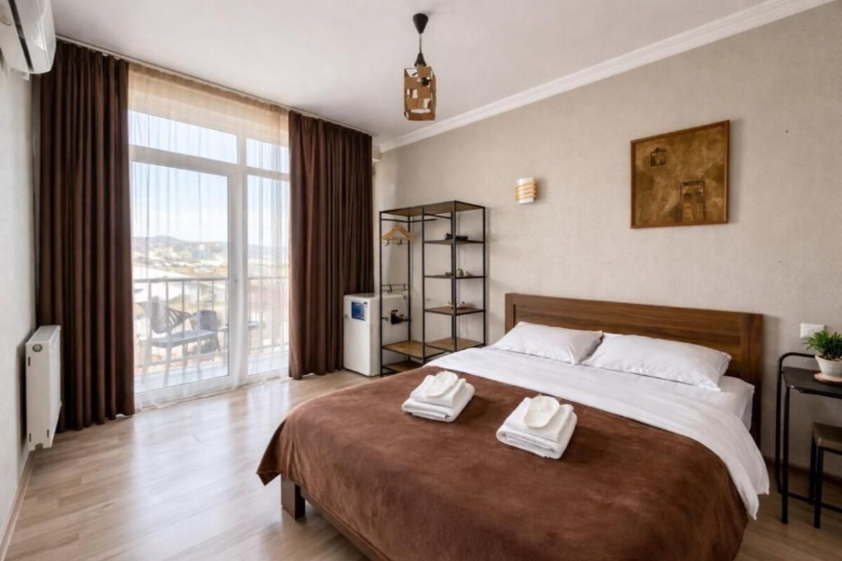 A hotel room with a large bed, a wardrobe, a desk, and a view of the outdoors.