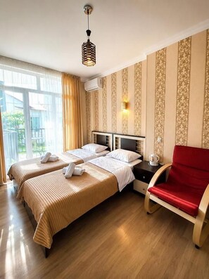 A hotel room with two beds, a red chair, and a window with curtains. - Hotel Marioni (tbilisi)