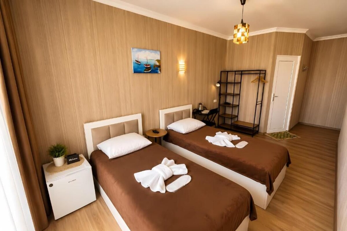 A hotel room with two beds, a nightstand, a small table, a wall-mounted shelf, and a door.