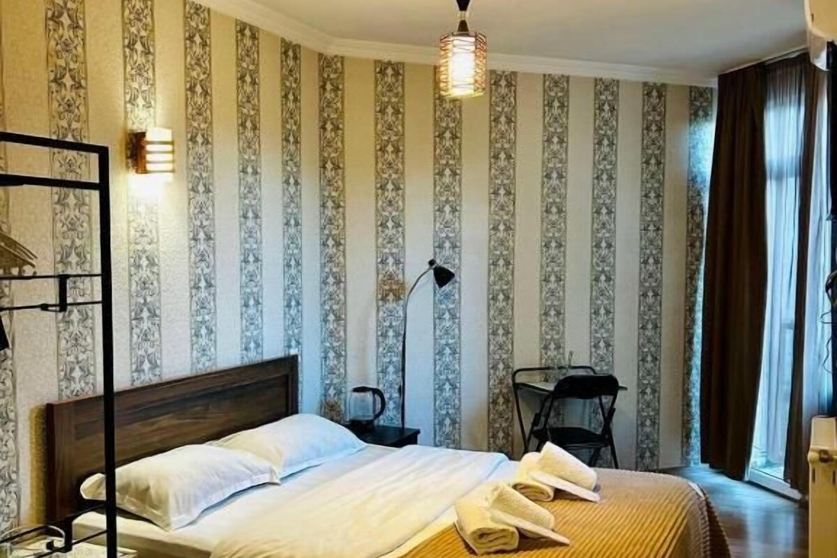 A hotel room with a bed, bedside table, lamp, and a window with curtains.