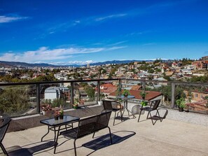 A rooftop terrace with a panoramic view of a cityscape, including buildings and mountains. - Hotel Marioni (tbilisi)