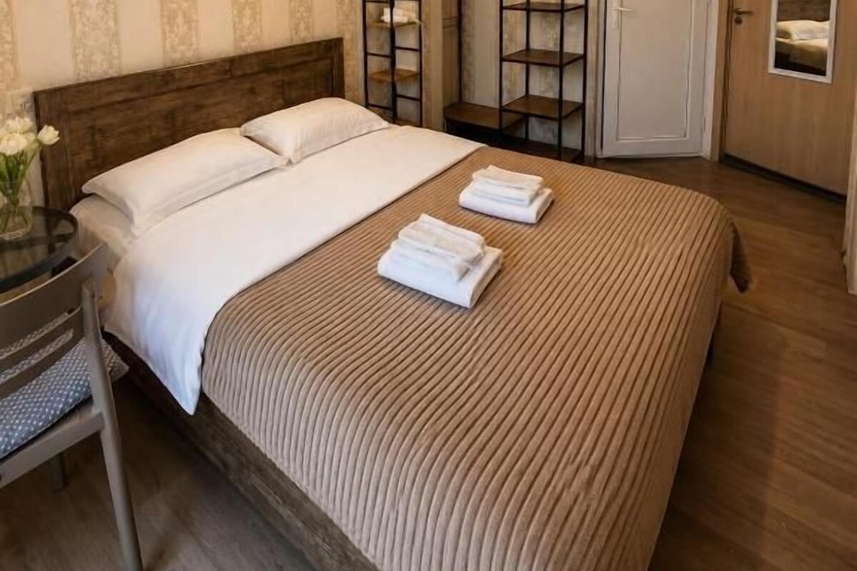 A hotel room with a large bed, bedside tables, a wardrobe, and a mirror.