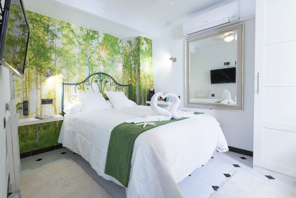 A hotel room with a bed, a mirror, a television, and a wall with a nature-themed mural. - Bed and Breakfast 'El Duende' with Shared Terrace, Wi-Fi and Air Conditioning (Cómpeta)