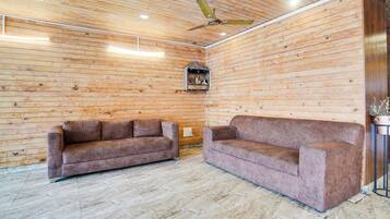 A room with wooden walls, two sofas, a ceiling fan, and a small decorative window.