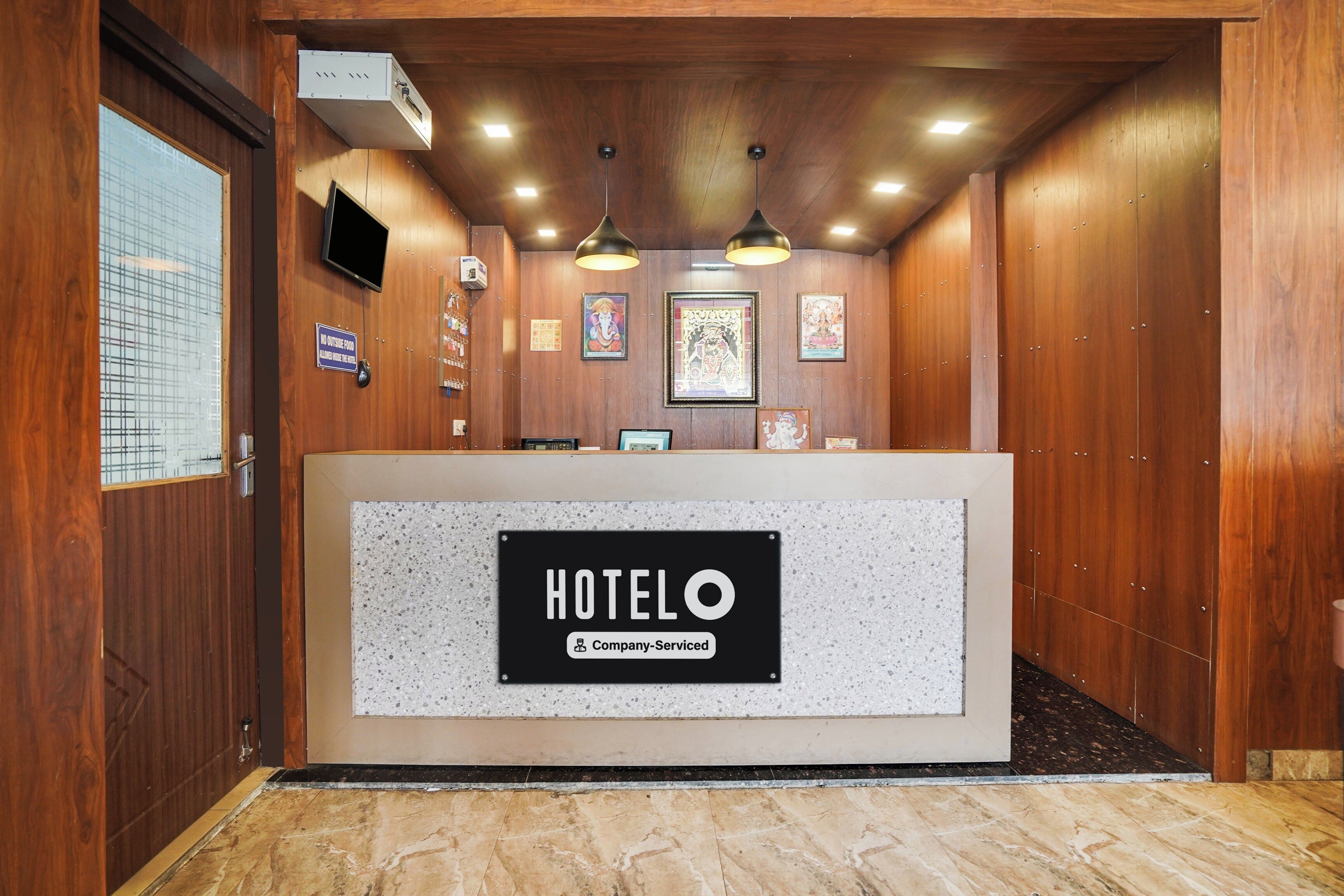 A hotel reception area with a reception desk, ceiling lights, and framed religious artwork.