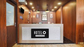 A hotel reception area with a reception desk, ceiling lights, and framed religious artwork.