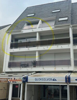 Un immeuble à plusieurs étages, doté de balcons et dont le rez-de-chaussée est occupé par un commerce.