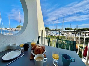 Een balkon met een tafel en ontbijtartikelen, uitzicht op een jachthaven met boten en een heldere lucht.
