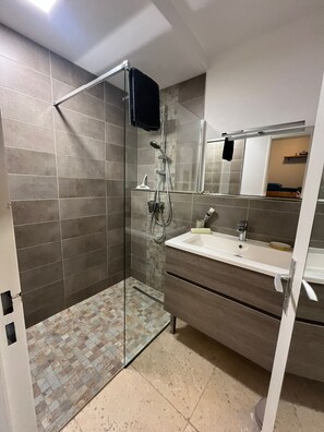 Een moderne badkamer met een douchecabine van glas, een wastafelmeubel met spiegel en een wastafel.