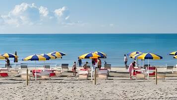 A beach with rows of beach chairs and umbrellas, a clear sky, and the ocean in the background.