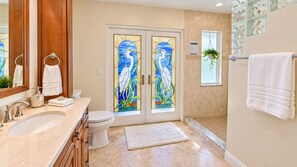 Une salle de bain avec un double lavabo, des toilettes et une porte en verre ornée d’un motif d’oiseau.
