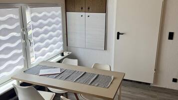 Una habitación con una mesa, dos sillas, una ventana con diseño ondulado, un armario de madera y una puerta.