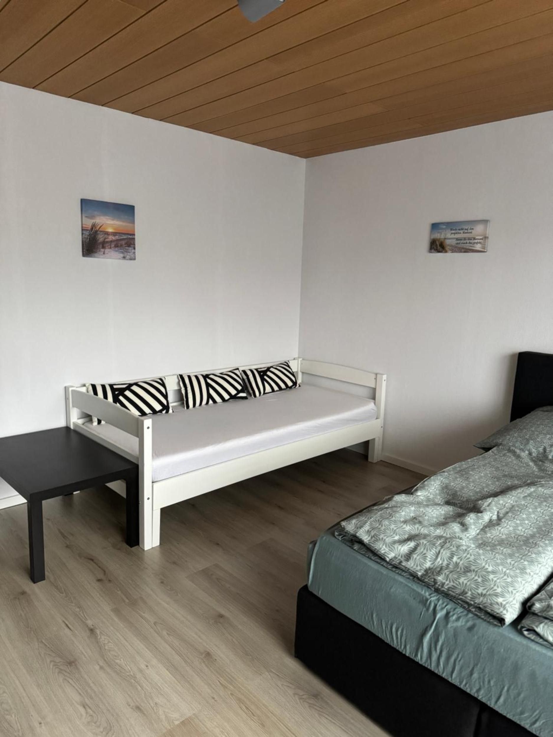 Una habitación con un sofá blanco, una mesita, una cama con colcha estampada y dos cuadros colgados en la pared.